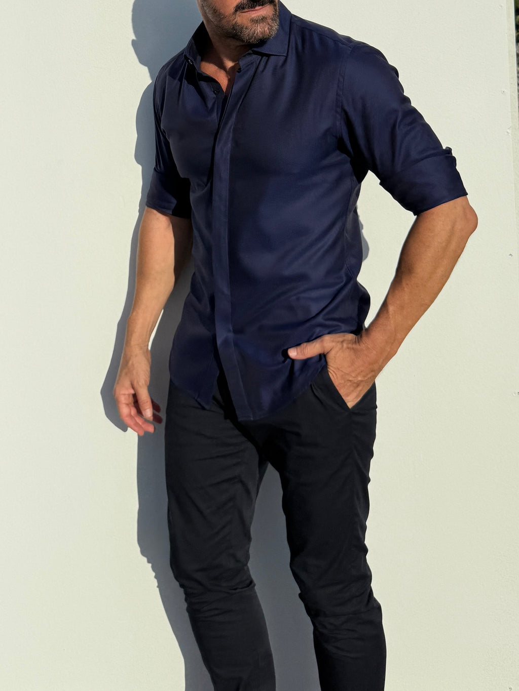 Man wearing a navy blue shirt and black pants against a light background