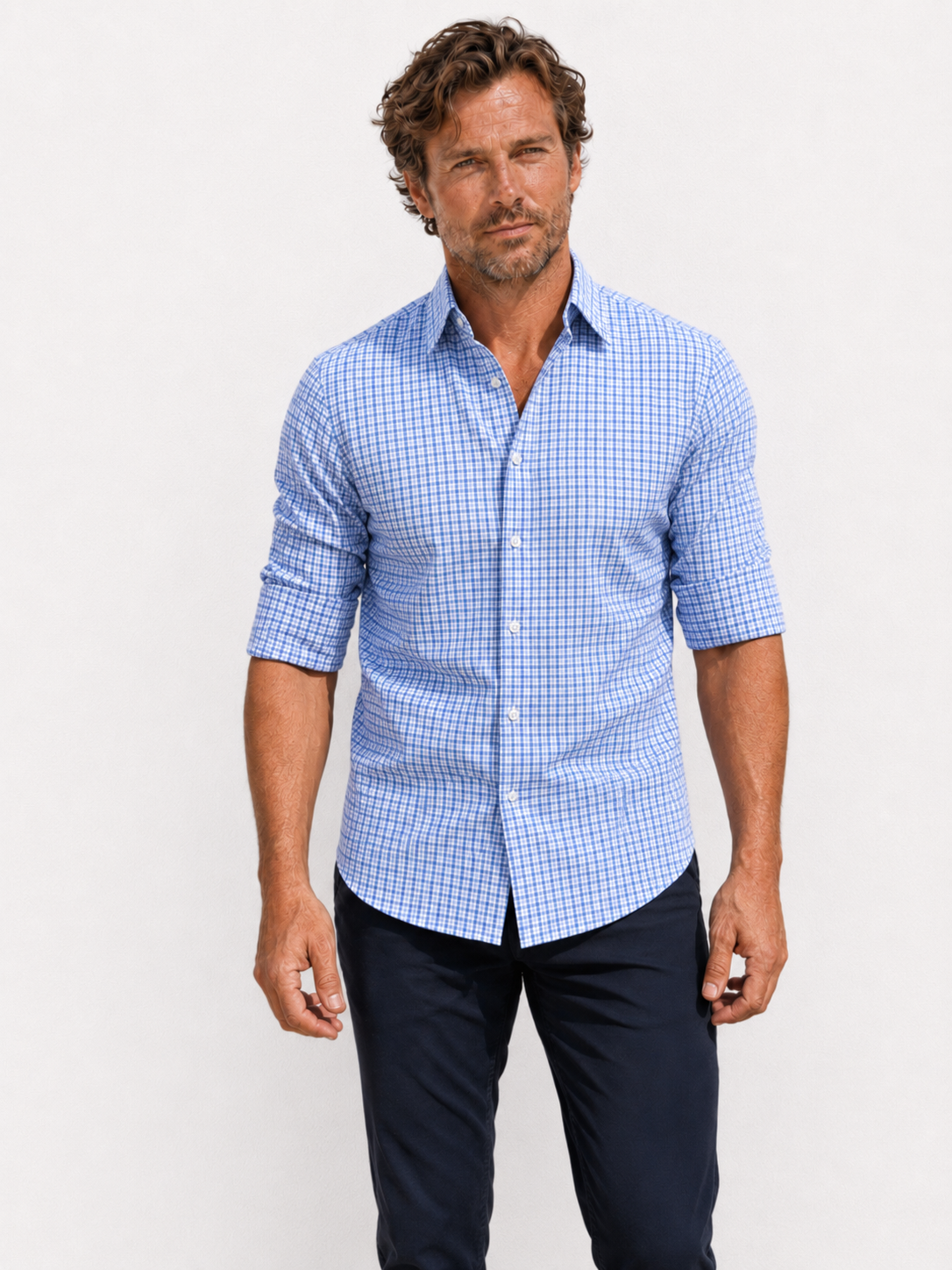 Man wearing a blue checkered shirt and dark pants against a white background
