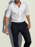 Man wearing a white dress shirt and black pants against a light background