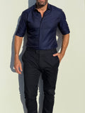 Man wearing a navy shirt and black pants against a light background
