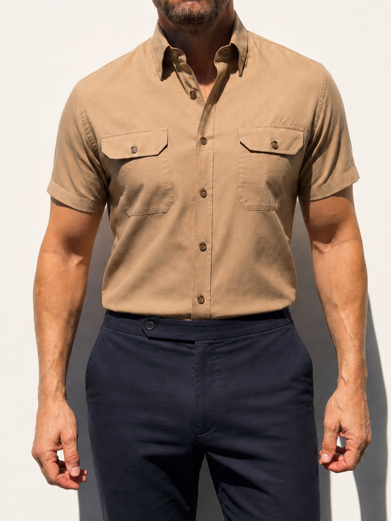 Man wearing a beige short-sleeve shirt and navy pants against a plain background