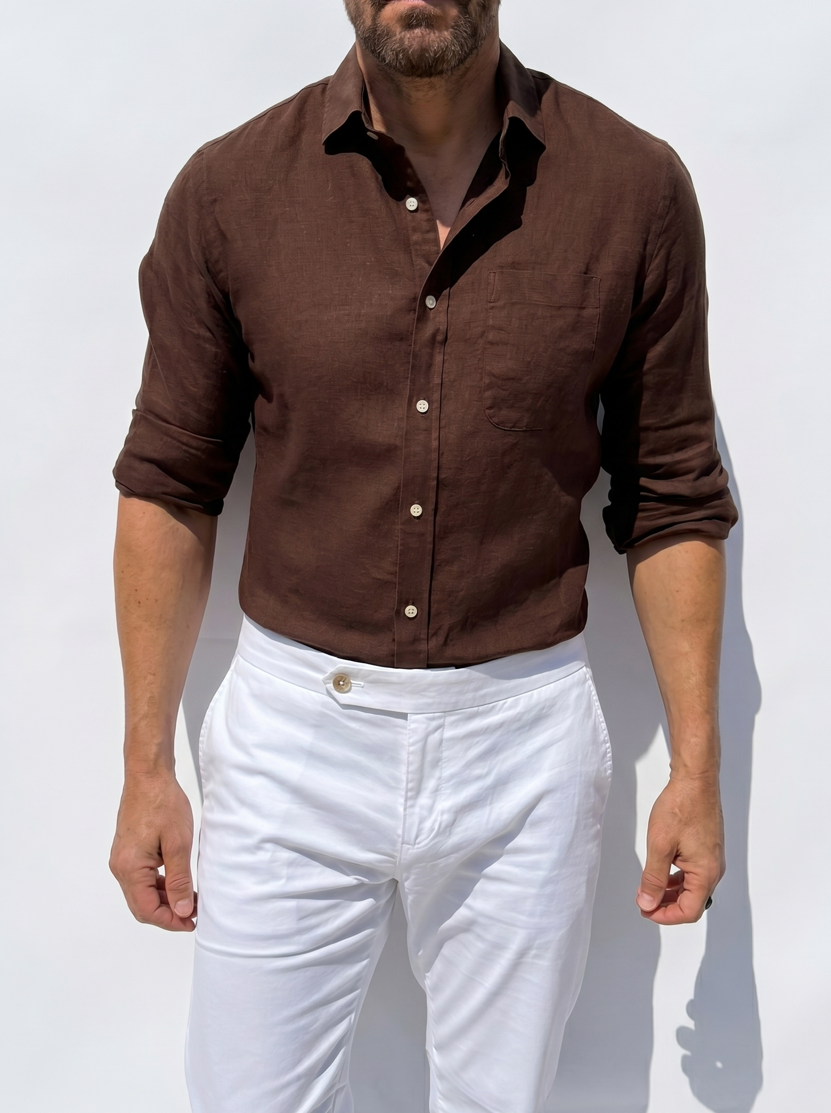 Man wearing a brown shirt and white pants against a light background