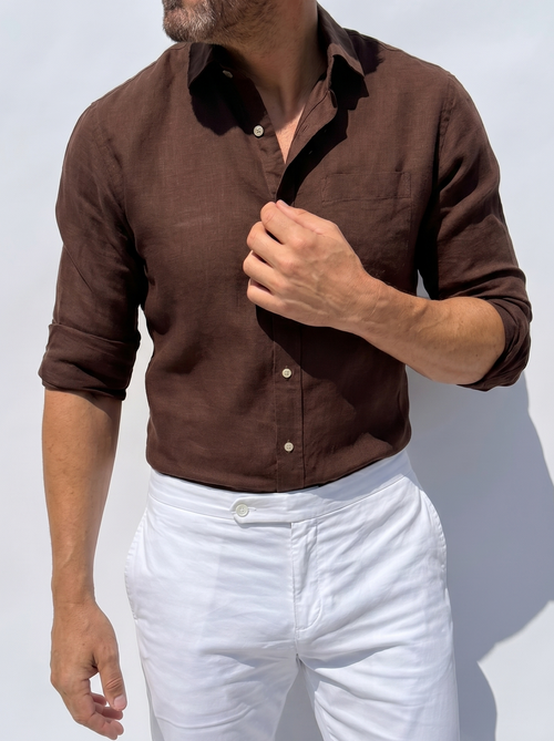 Man wearing a brown shirt and white pants against a light gray background