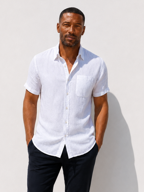 Man wearing a white shirt and black pants against a white wall.