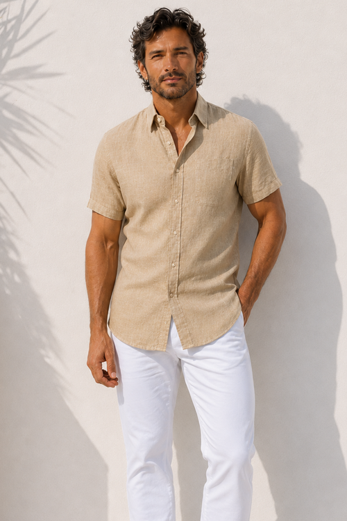 Man wearing a beige shirt and white pants against a white wall.