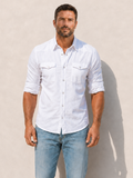 Man wearing a white shirt and light blue jeans against a beige wall.
